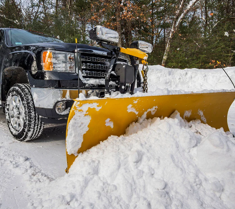 A snow plow is parked next to a black truck